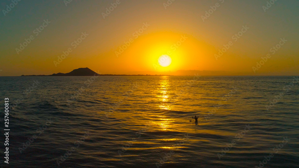 AERIAL Man sitting on his surfboard and outstretches his arms at stunning sunset AERIAL Man sitting on his surfboard and outstretches his arms at stunning sunset