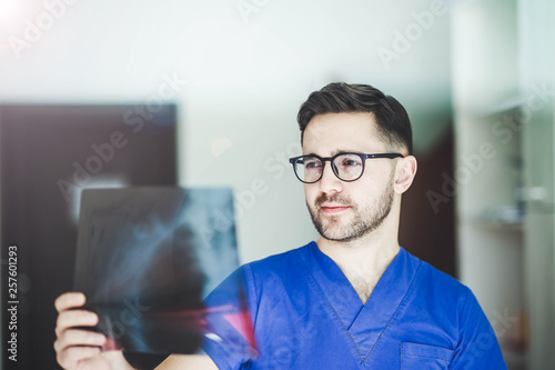 young man doctor with glasses, a radiologist, a surgeon examines a x-ray of a patient.