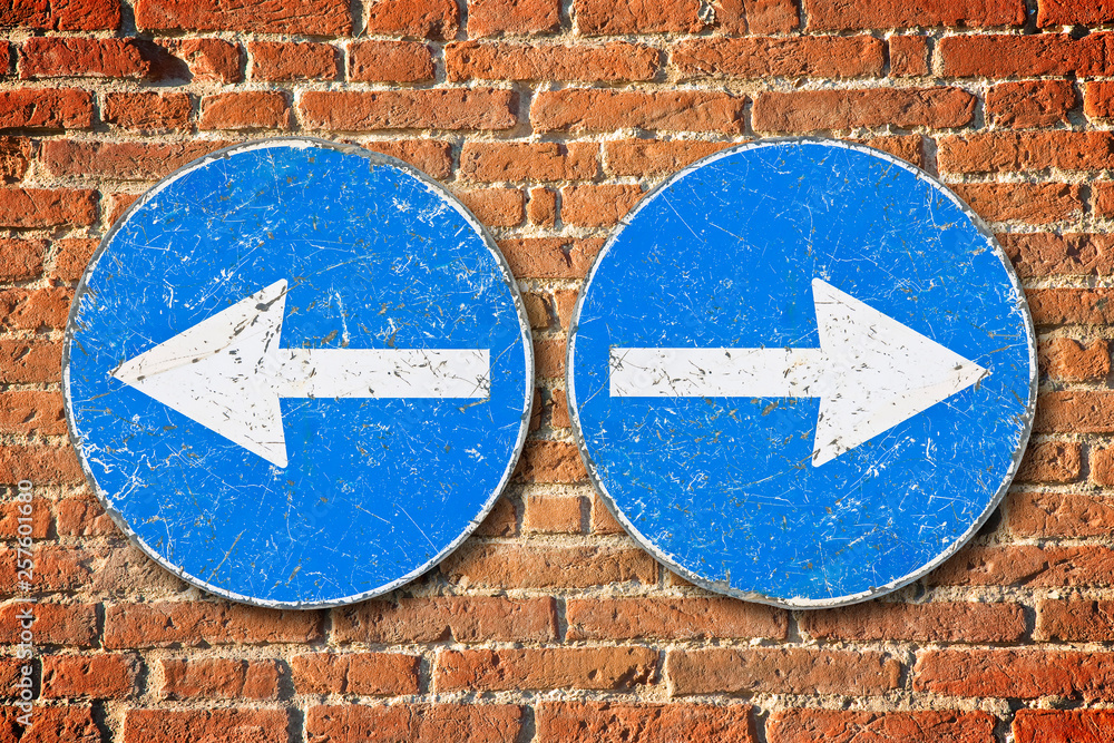 Old blue metallic arrow sign against an aged brick wall indicating to go left and right - concept image Old blue metallic arrow sign against an aged brick wall indicating to go left and right - concept image