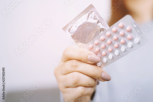Cuadro en lienzo Contraceptive means: Woman hand holding contraceptive pills and condom sitting on sofa background