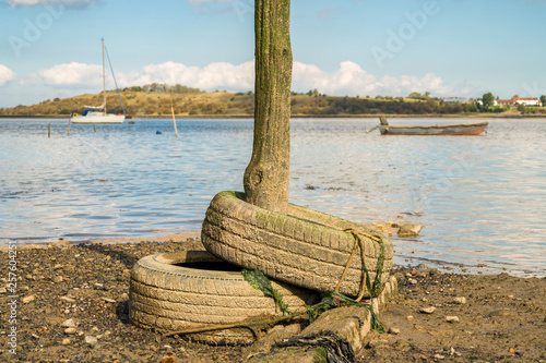 Old tyres and a wooden post in the Oare Marshes near Faversham, Kent, England, UK - with boats and the Isle of Sheppey in the background photo