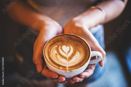 woman hold a cup of latte art coffee in hand at cafe, vintage tone  photo