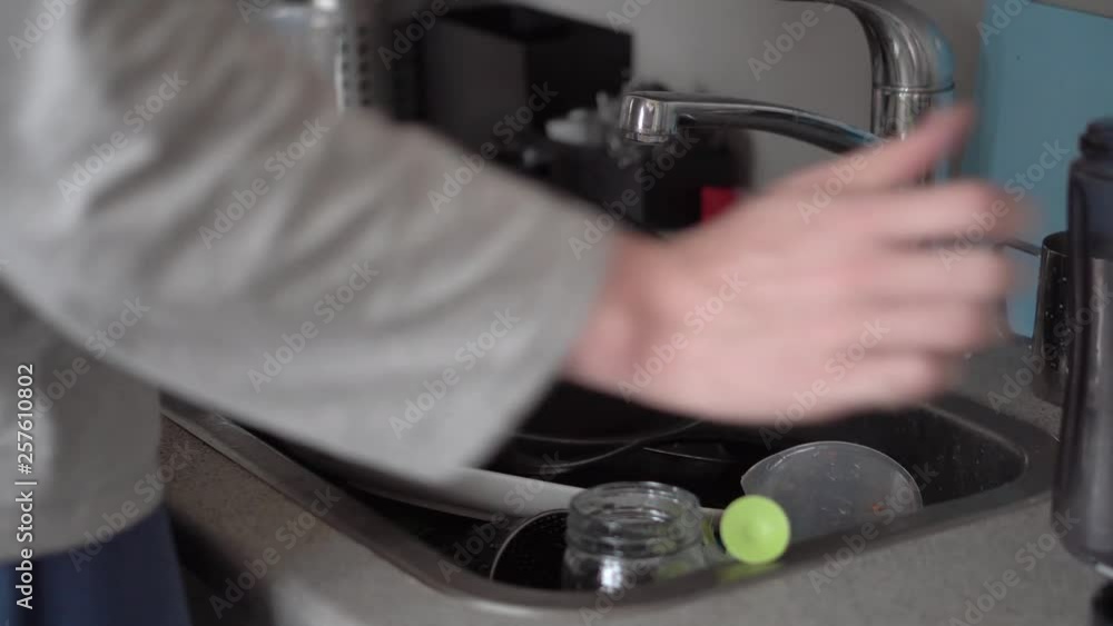 A student man in pyjamas washes and dries a dirty pan in a sink of dirty plates, cups and dishes A student man in pyjamas washes and dries a dirty pan in a sink of dirty plates, cups and dishes