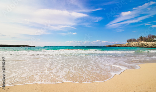 Salento beach, Taranto, Puglia, Italy, waves breaking on the coast and isolated stones on the sand, partly cloudy blue sky