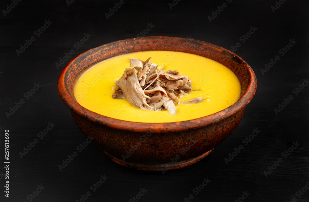 Pumpkin soup with Chiken in a clay plate on black background. Pumpkin soup with Chiken in a clay plate on black background.
