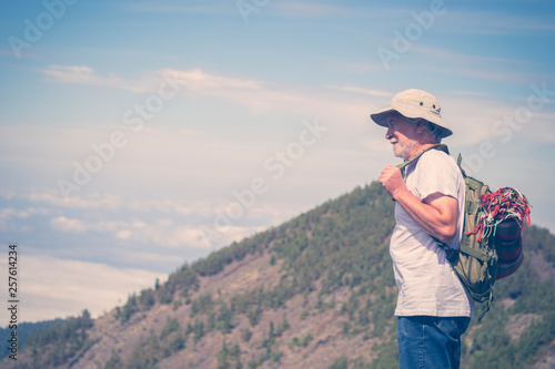 Retired lifestyle mature man with backpack traveling and enjoying the outdoor leisure activity on the top of a mountain looking the sky and the landscape with satisfaction © simona
