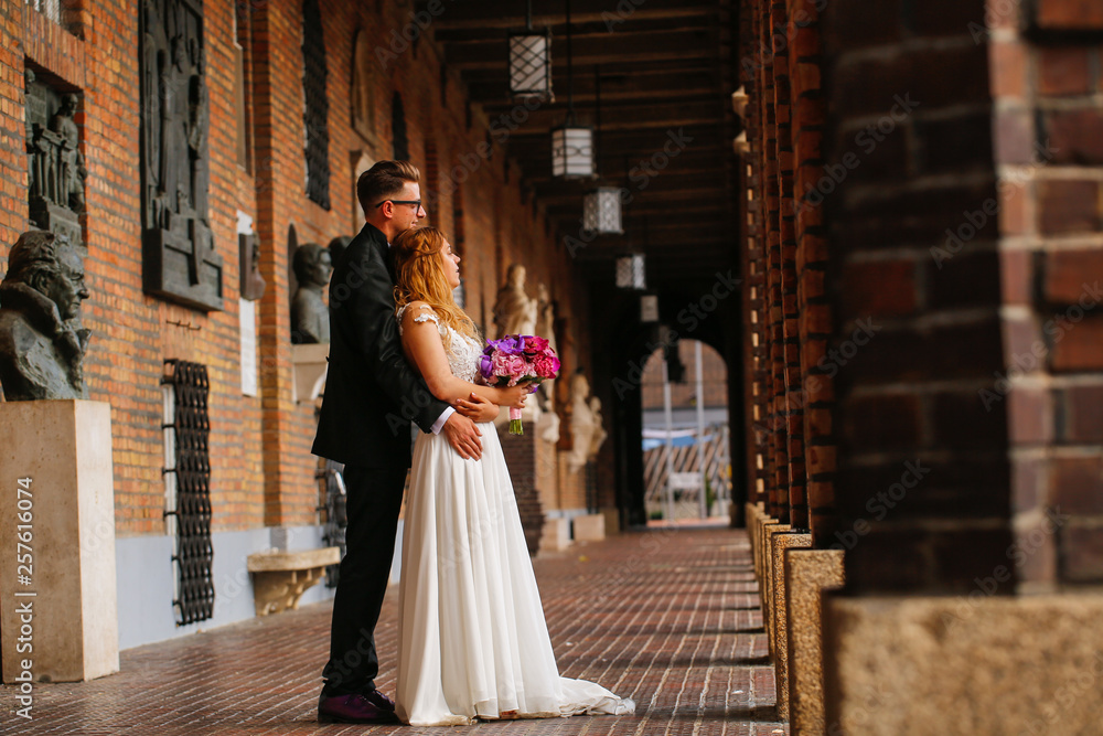 Beautiful wedding couple posing in city, bride holding beautiful bouquet of flowers in hands Beautiful wedding couple posing in city, bride holding beautiful bouquet of flowers in hands