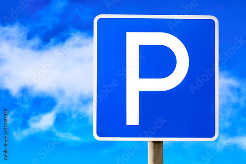 Blue parking sign against blue cloudy sky background.
