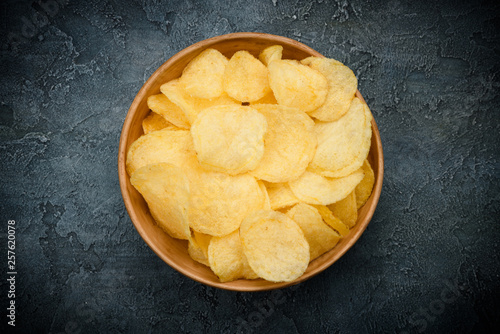 Crispy potato chips fried with olive oil and salted in bowl on dark table