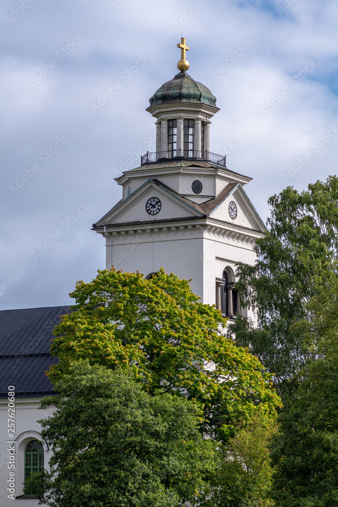 White church tower with lush green trees in sunlight