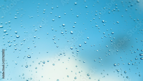 Water drops on the window, blue sky and clouds in the blurry background.