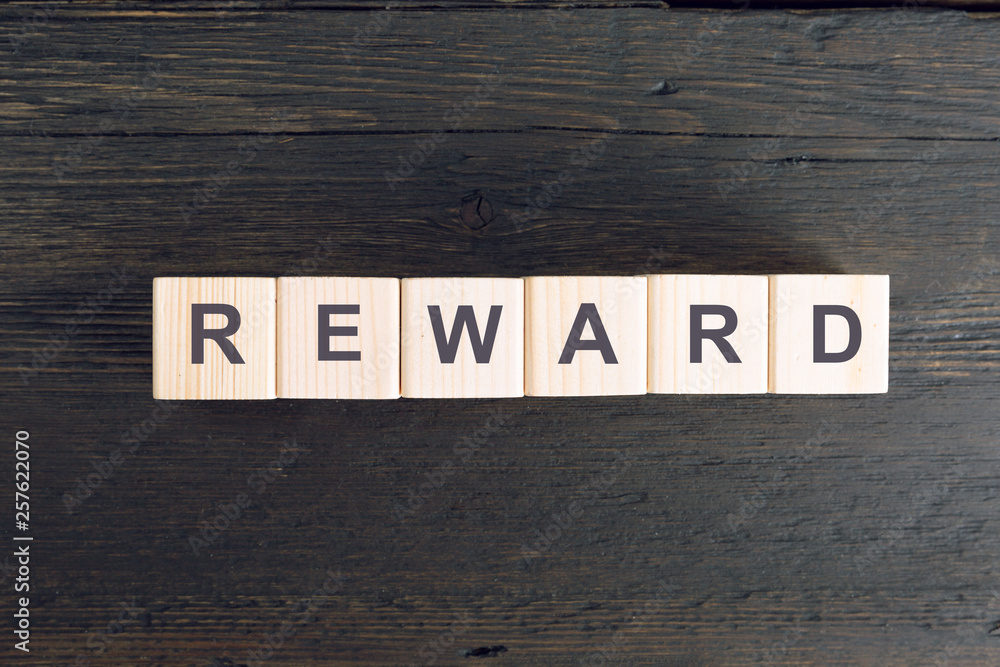 Fototapeta premium Word REWARD written on a wooden cube. Risk and reward concept