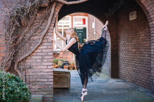 Young ballerina in ballet costume dancing and pointe shoes is in a beautiful pose dancing on the street. 