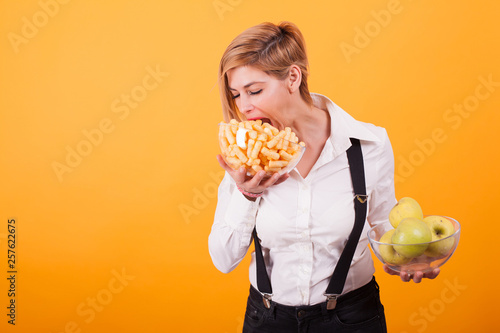 Pretty blond woman with short hair taking a bite from her corn puffs over yellow background.