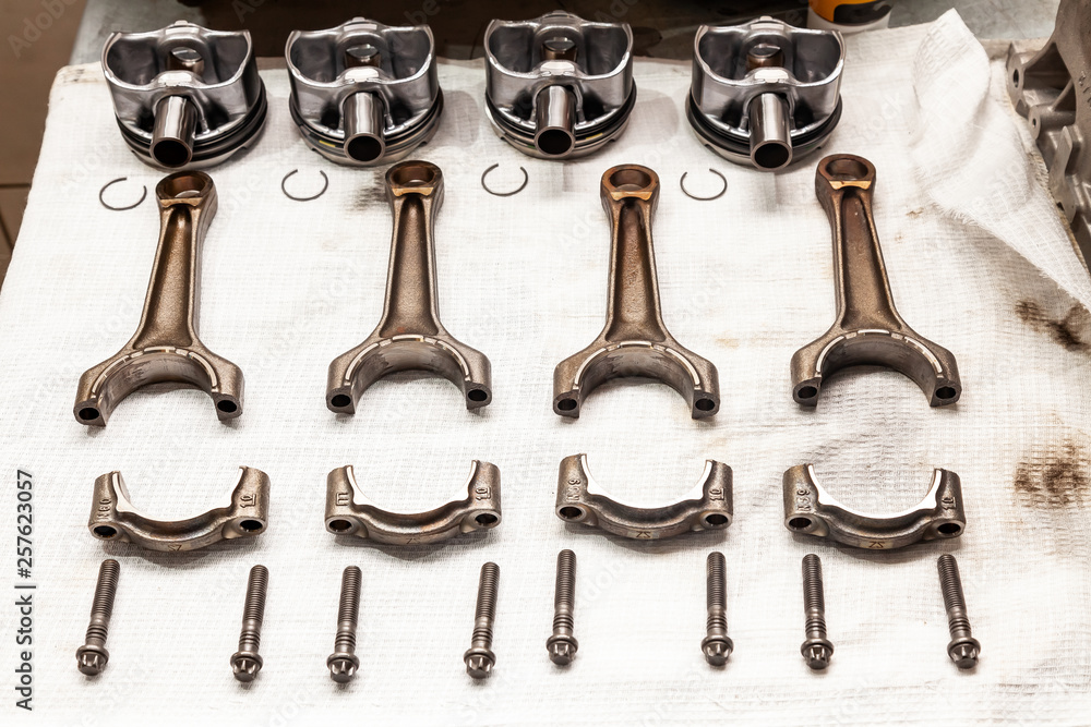 Engine connecting rods and pistons used and removed from a four-cylinder engine on a white soft cloth in a vehicle repair workshop. Auto service industry.