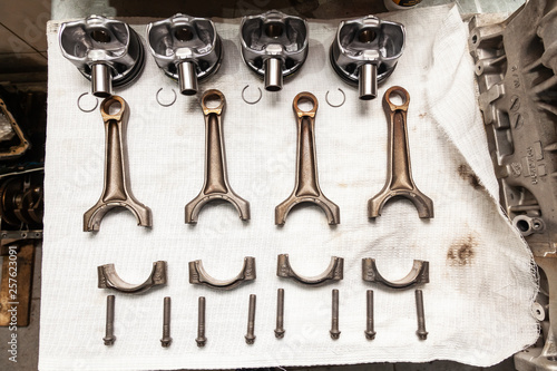 Engine connecting rods and pistons used and removed from a four-cylinder engine on a white soft cloth in a vehicle repair workshop. Auto service industry.