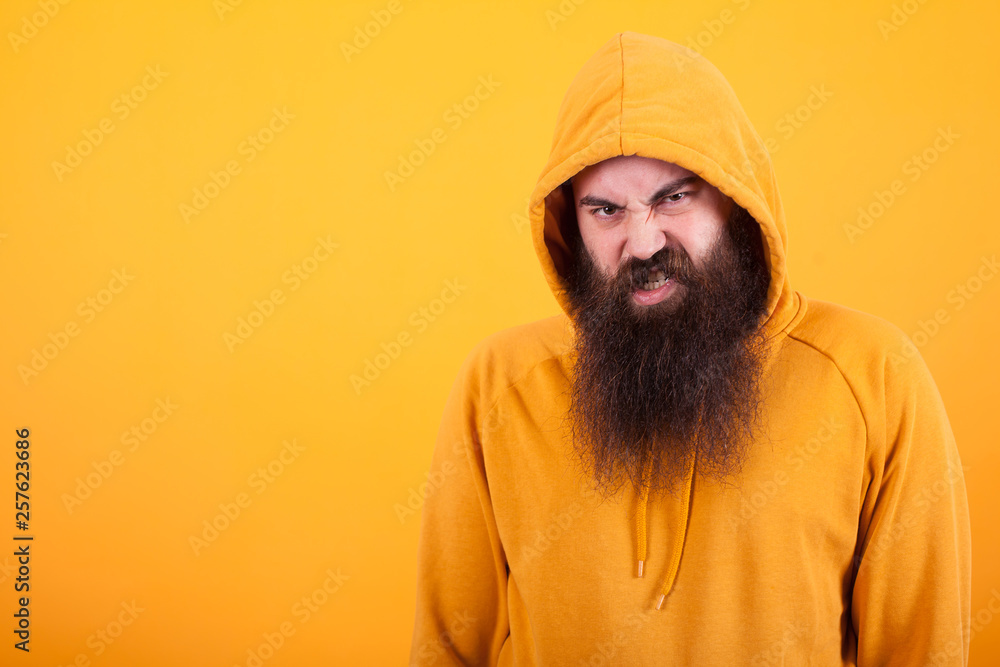 Cool bearded hipster looking at the camera with angry face over yellow background Cool bearded hipster looking at the camera with angry face over yellow background