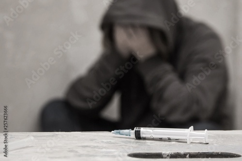 Syringe with out of focus man drug addict sitting in the background photo