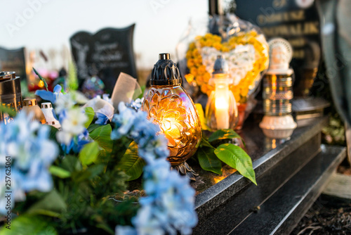 Artificial and real flowers and lit candles lying on the tombstone in the cemetery. © Michal