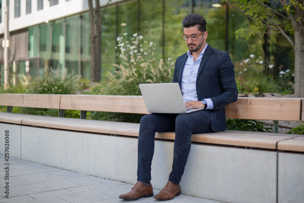 Handsome young businessman working outside on his laptop