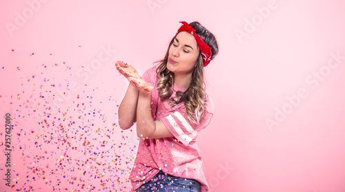 Funny girl in a pink t-shirt with balloons and confetti gives a smile and emotions on a pink background