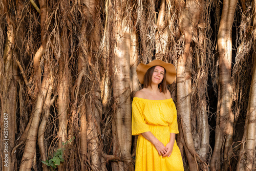 Girl in a yellow dress and hat against the backdrop of tropical wood