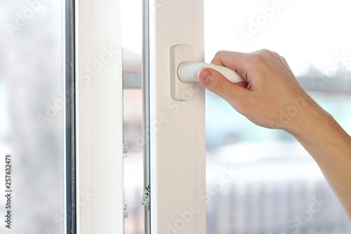 A man's hand opens a white plastic window. Close up
