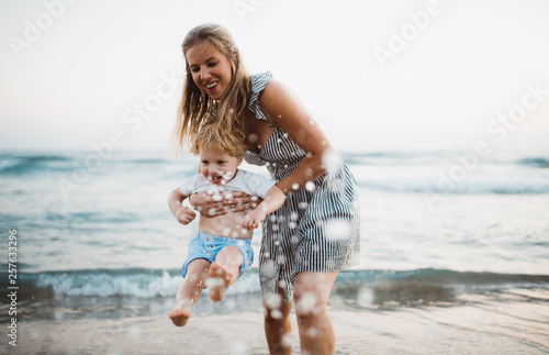 Canvas Print Young mother with a toddler boy standing on beach on summer holiday, having fun