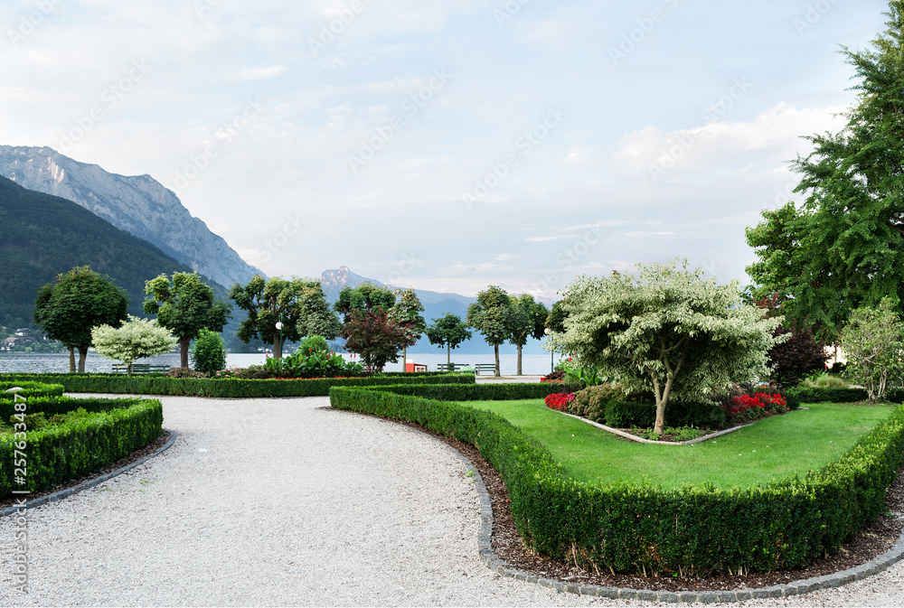 View of the mountains, the lake and the embankment of the city with trimmed trees, shrubs, lawn and flower beds. View of the mountains, the lake and the embankment of the city with trimmed trees, shrubs, lawn and flower beds.