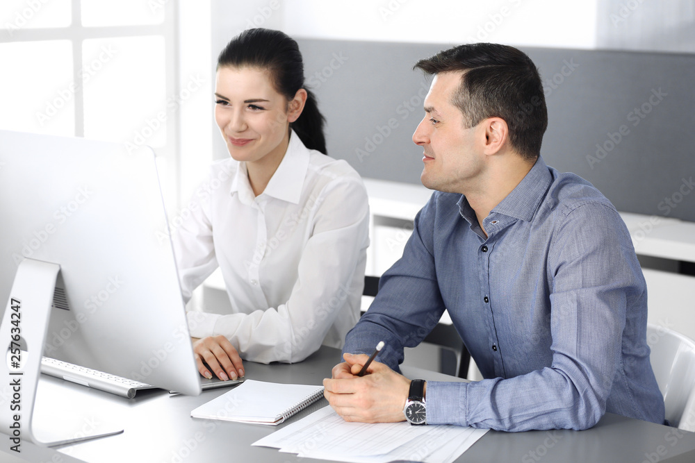 Cheerful smiling businessman and woman working with computer in modern office. Headshot at meeting or workplace. Teamwork, partnership and business concept Cheerful smiling businessman and woman working with computer in modern office. Headshot at meeting or workplace. Teamwork, partnership and business concept