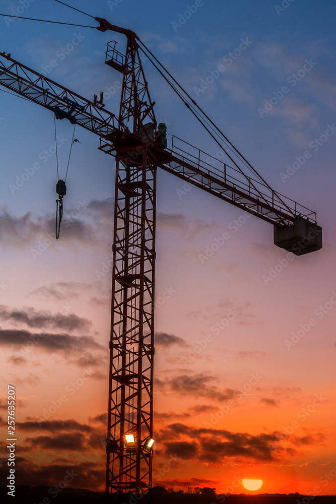 Silhouette of a crane in a construction at orange sunrise