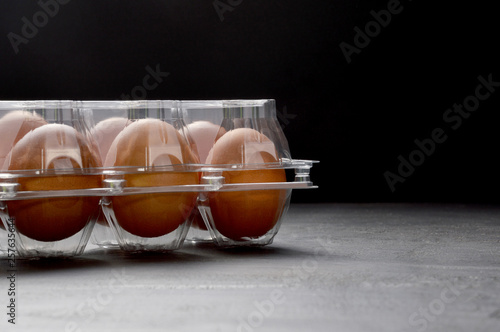 Brown eggs in a transparent plastic box on black background