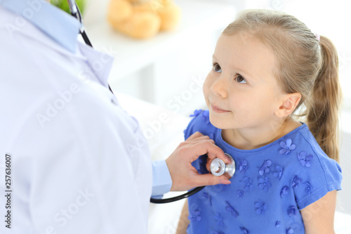 Doctor examining a little girl by stethoscope. Happy smiling child patient at usual medical inspection. Medicine and healthcare concepts