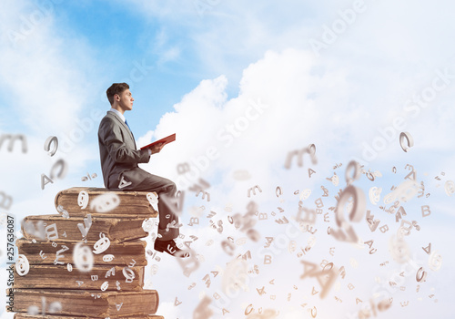 Man student on stack reading book and symbols flying around