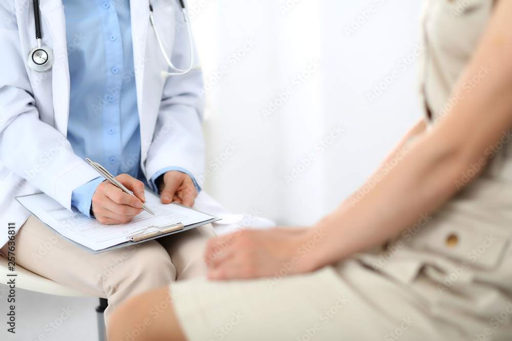 Doctor and patient talking. Physician at work in hospital while writing up medication history records form on clipboard near sitting woman. Healthcare and medicine concepts