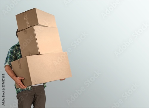 Fotografie Delivery man carrying stacked boxes in front of face against  background