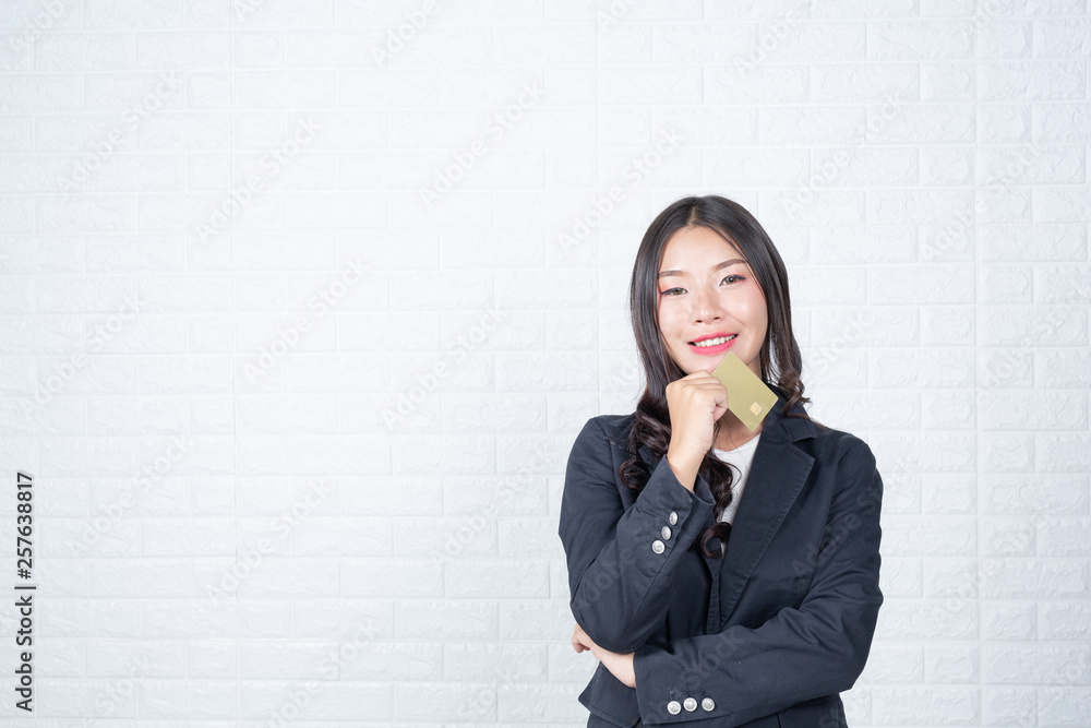Business woman holding a separate cash card, white brick wall Made gestures with sign language. Business woman holding a separate cash card, white brick wall Made gestures with sign language.