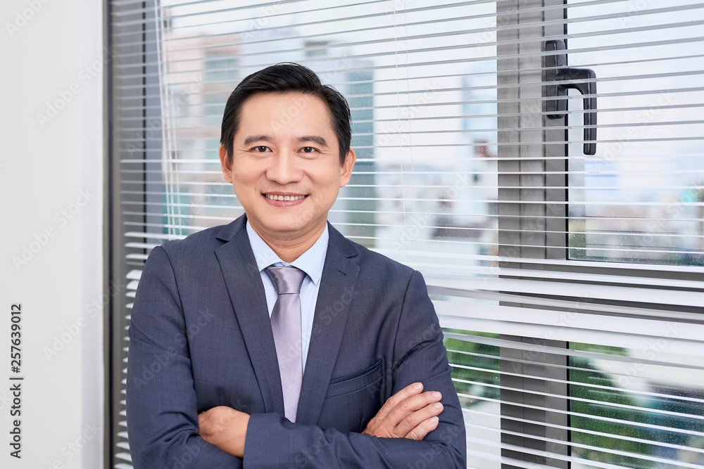 Single confident and handsome male businessman in blue suit and necktie with grin leaning on window outdoors Single confident and handsome male businessman in blue suit and necktie with grin leaning on window outdoors
