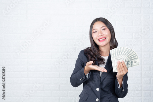 A young businesswoman holds a dollar note on a white brick wall background. photo