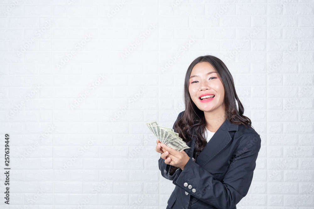 A young businesswoman holds a dollar note on a white brick wall background. A young businesswoman holds a dollar note on a white brick wall background.