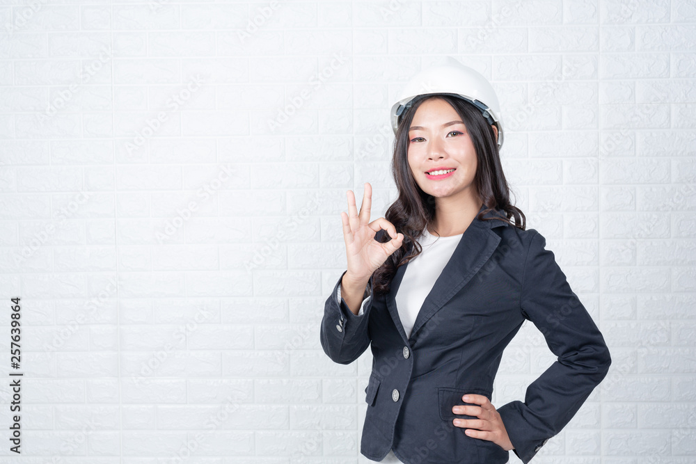 Woman of engineering holding a hat, Separate the white brick wall made gestures with sign language. Woman of engineering holding a hat, Separate the white brick wall made gestures with sign language.