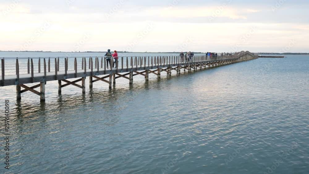 Lesina, Gargano National Park, Apulia, Italy - March 11 2019: people walk on jatty on (lake) lagoon at sunset. the red color of the twilight on the lagoon creates a beautiful effec Lesina, Gargano National Park, Apulia, Italy - March 11 2019: people walk on jatty on (lake) lagoon at sunset. the red color of the twilight on the lagoon creates a beautiful effec