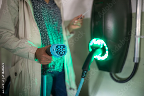 Young woman charging an electric vehicle in an underground garage equiped with e-car charger. Car sharing concept. photo