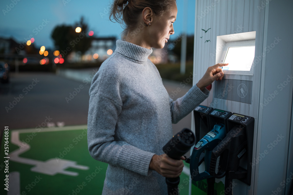 Young woman charging an electric vehicle. Car sharing concept. Young woman charging an electric vehicle. Car sharing concept.