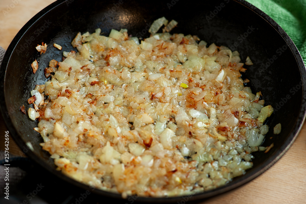 Fried onion in the pan. Macro. Cook onions in a pan for a dish. Stewed onions close-up. Cooking vegetables in a pan.