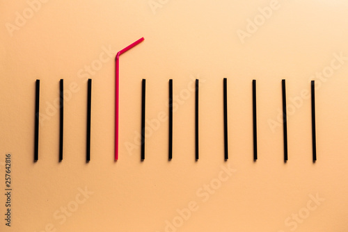 Red cocktail straw among black ones on color background. Concept of uniqueness