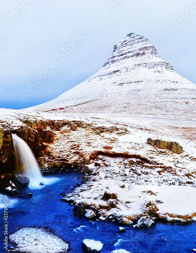 View of the Kirkjufell Mountain and Kirkjufellsfoss waterfall in Iceland on a cloudy day in winter.