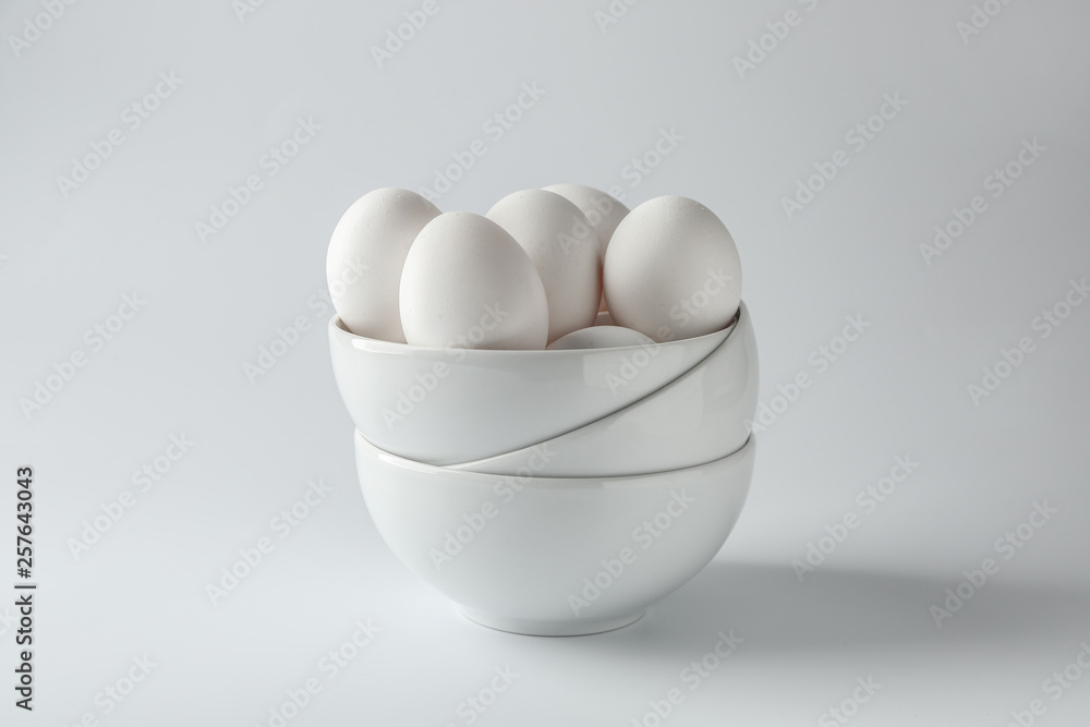 Bowls with tasty raw eggs on white background