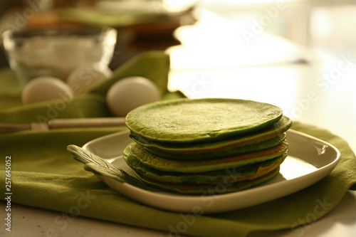 Plate with tasty green pancakes on table in kitchen