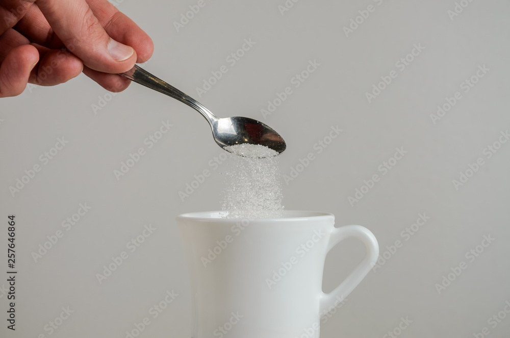 A hand spooning sugar in a white mug A hand spooning sugar in a white mug